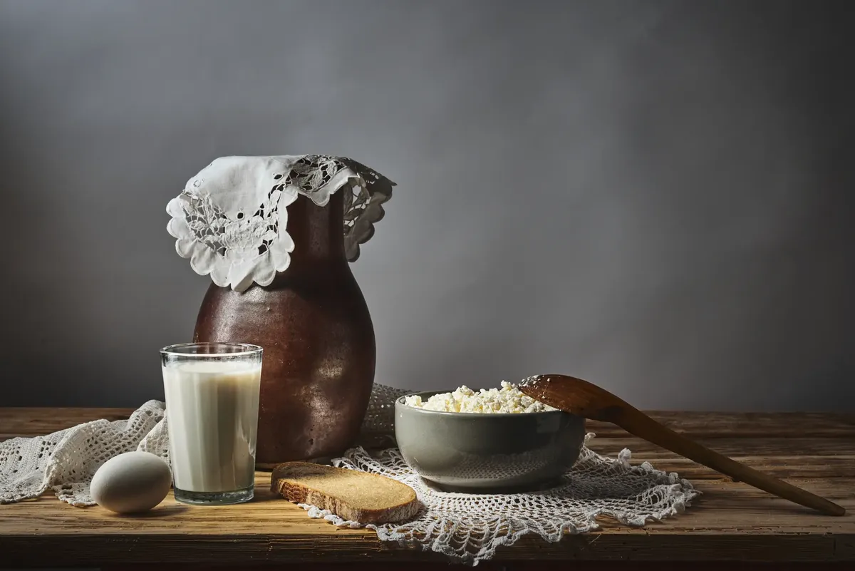 Rustic dairy still life featuring milk, cottage cheese, and bread on a wooden table.