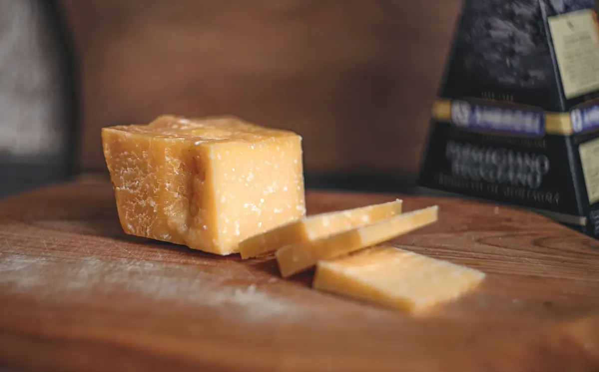 A detailed view of Parmigiano Reggiano cheese with slices on a wooden surface.